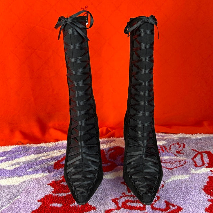 Black high-heeled shoes with decorative bows on a red and white patterned surface.