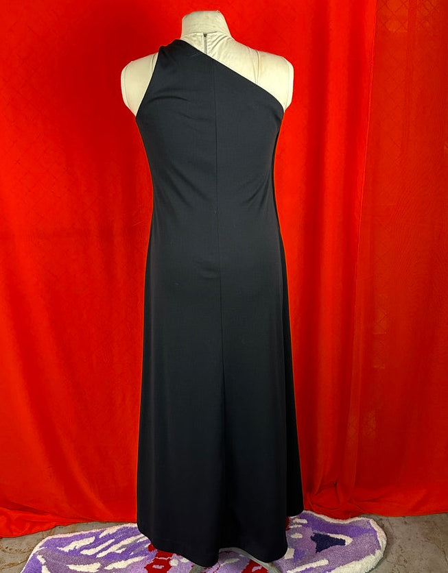 Black one-shoulder dress on a mannequin against an orange curtain background