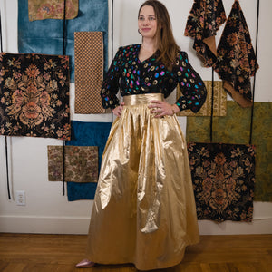 young lady wearing a Jessica McClintock lame ball gown skirt and multicolored top in front on a wall with hanging fabrics. 