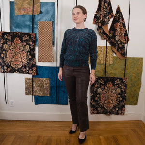 young lady wearing crocodile print leather pants with paisley wool sweater in front of a wall with various hanging fabrics